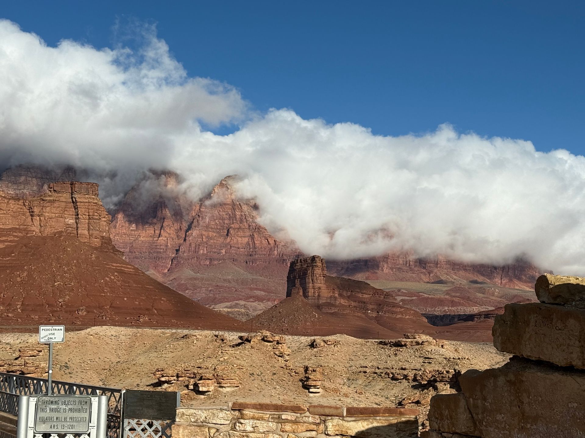 Red rock mountains partially obscured by white clouds under a blue sky. Desert landscape.