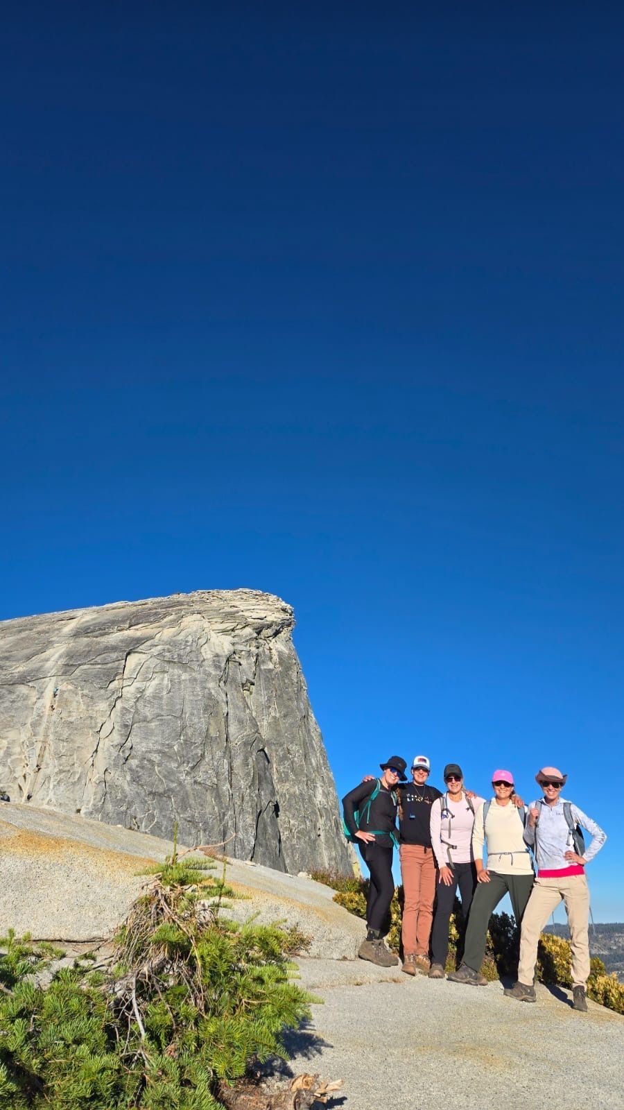 Group poses atop a rocky summit under a clear, blue sky.