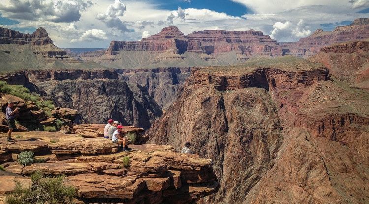A group of people are sitting on top of a rocky cliff overlooking a canyon.