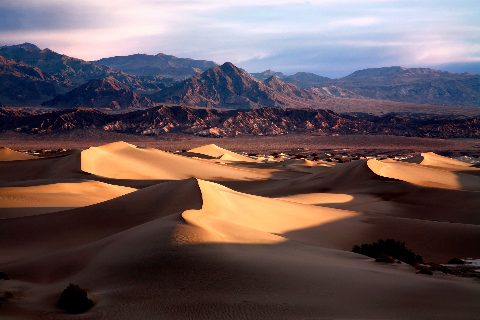 Sunlit sand dunes with mountains in the background under a pink-blue sky