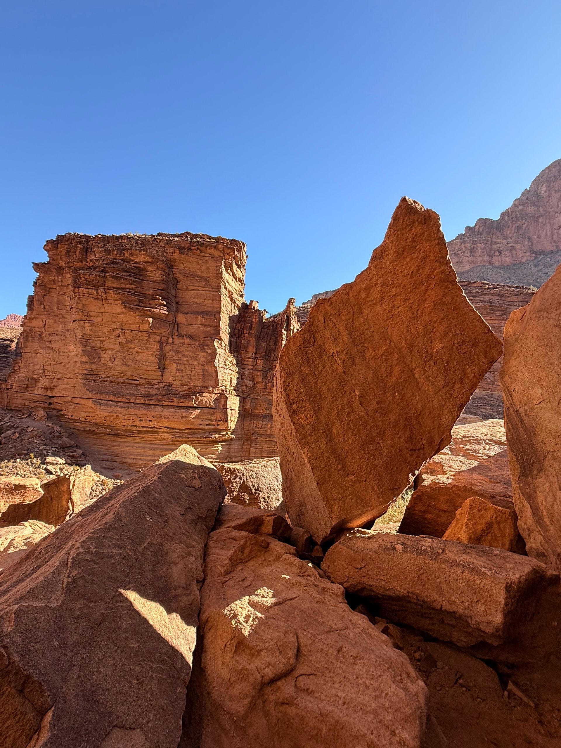 Red rock formations under a clear blue sky, casting shadows on the uneven ground.