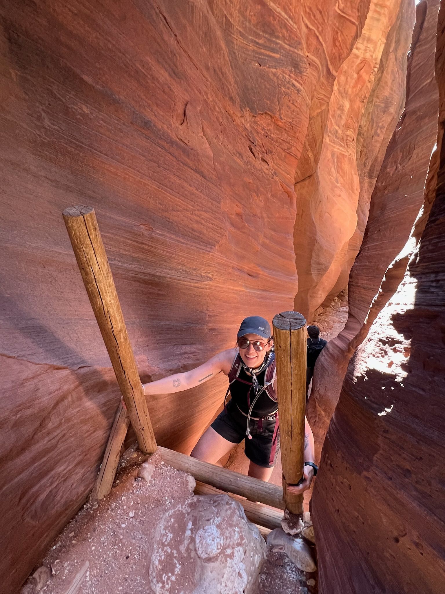 Person climbs wooden ladder in a narrow slot canyon with red rock walls.