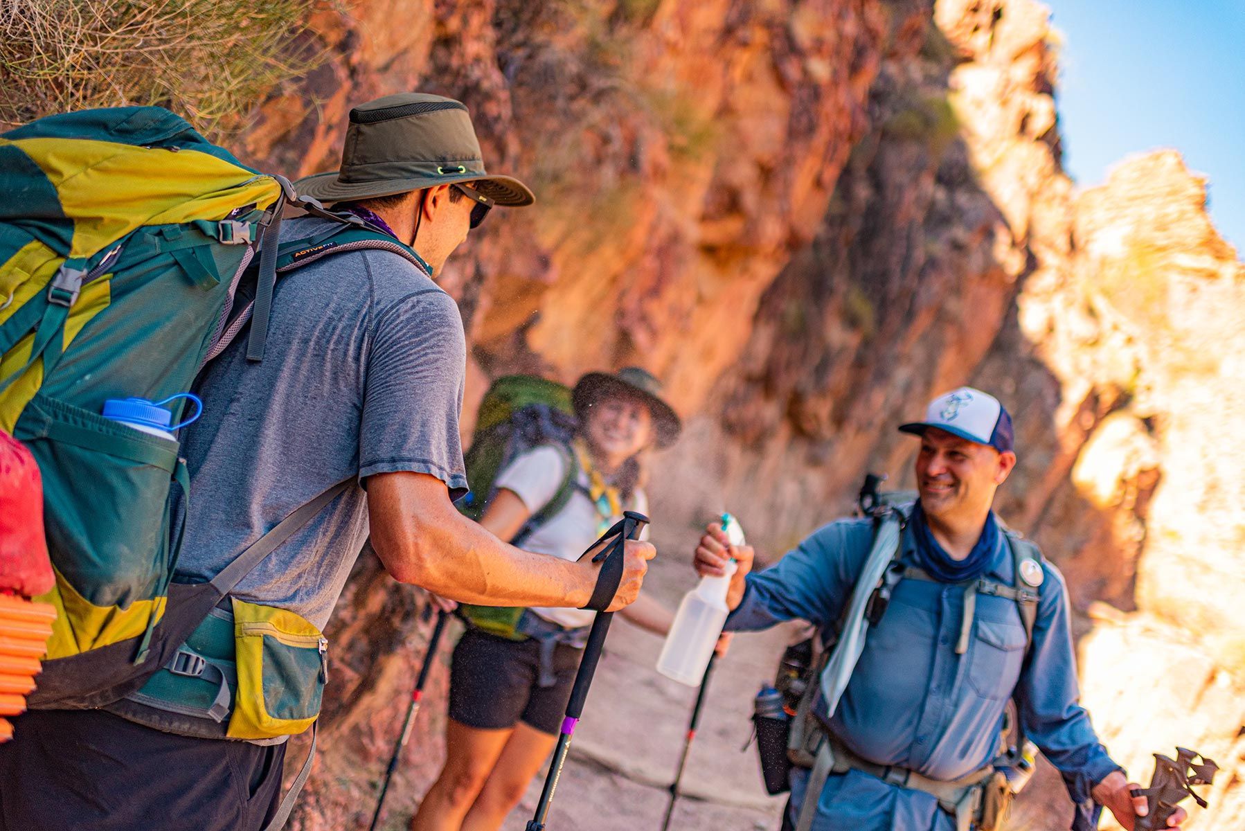 Hikers with backpacks and trekking poles talking on a sunlit canyon trail