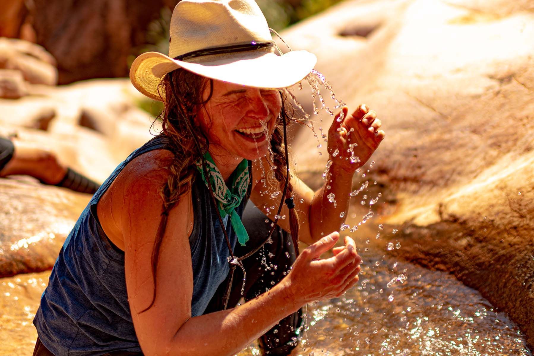 A woman drinking water from a bottle with mountains in the background