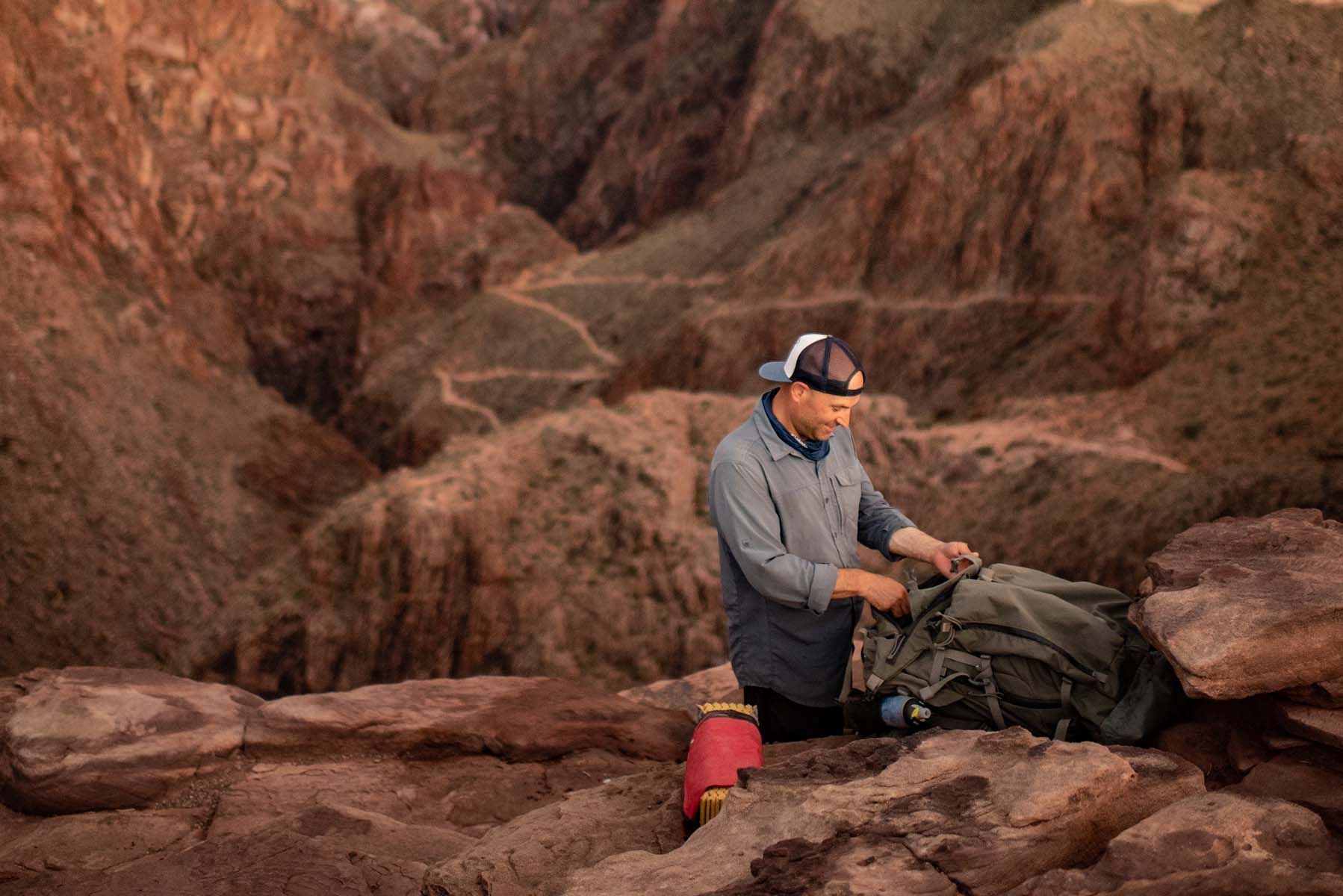 Hiker in gray jacket packing gear on red rocks in a desert canyon