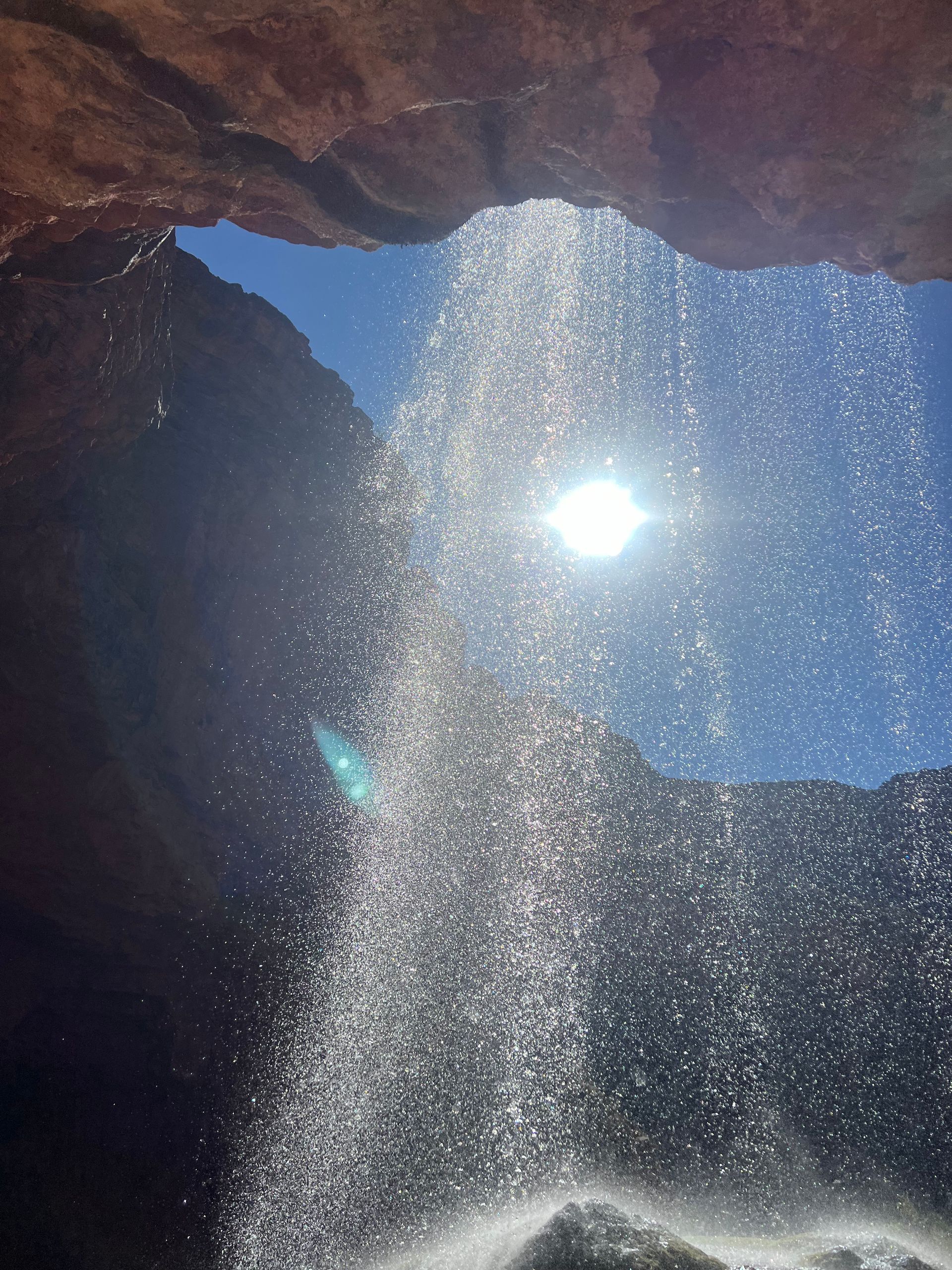 A waterfall in a cave with the sun shining through it