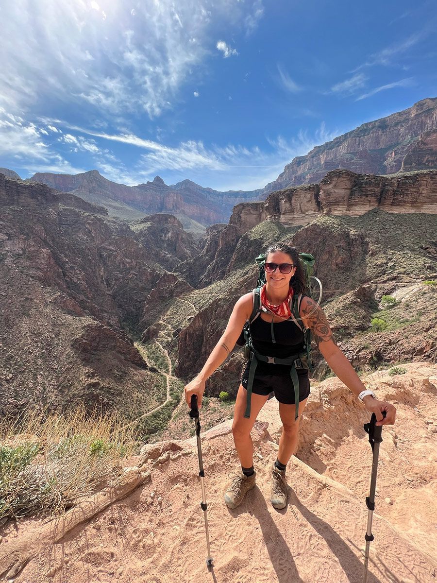Hiker with trekking poles climbing a rocky desert trail in a mountain canyon under a blue sky