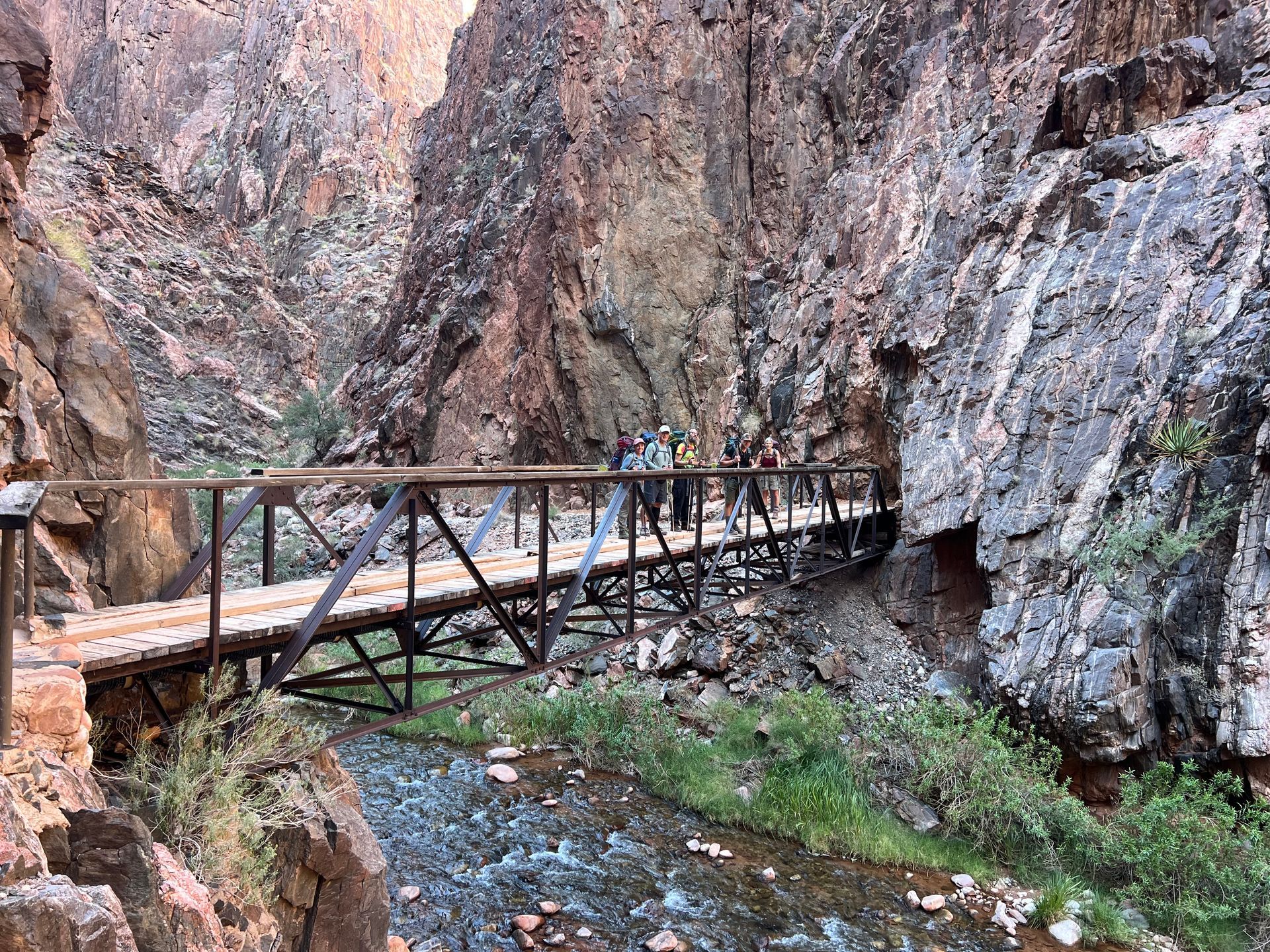 A group of people are walking across a wooden bridge over a river.