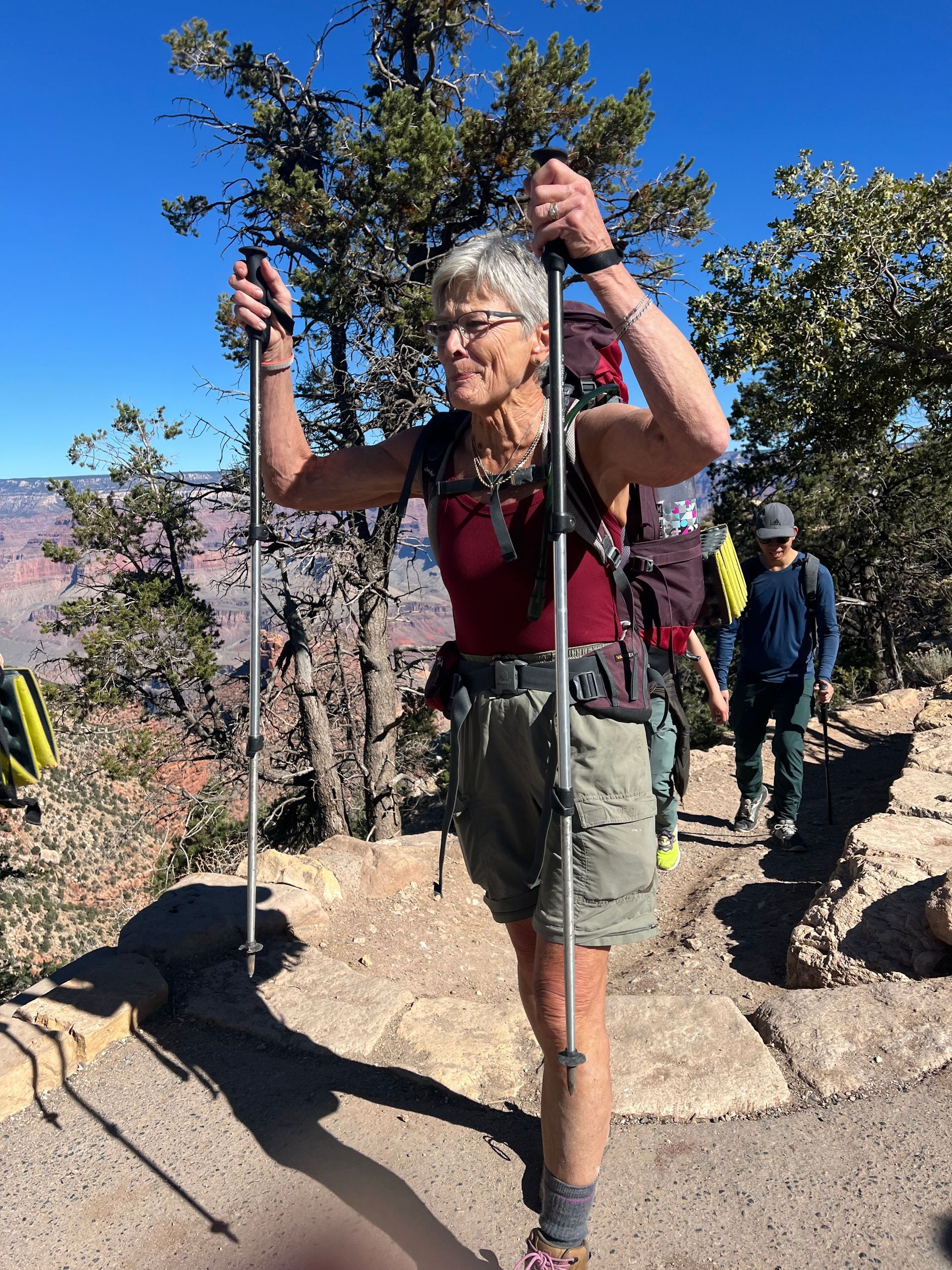 A woman with a backpack and hiking poles is walking on a trail.