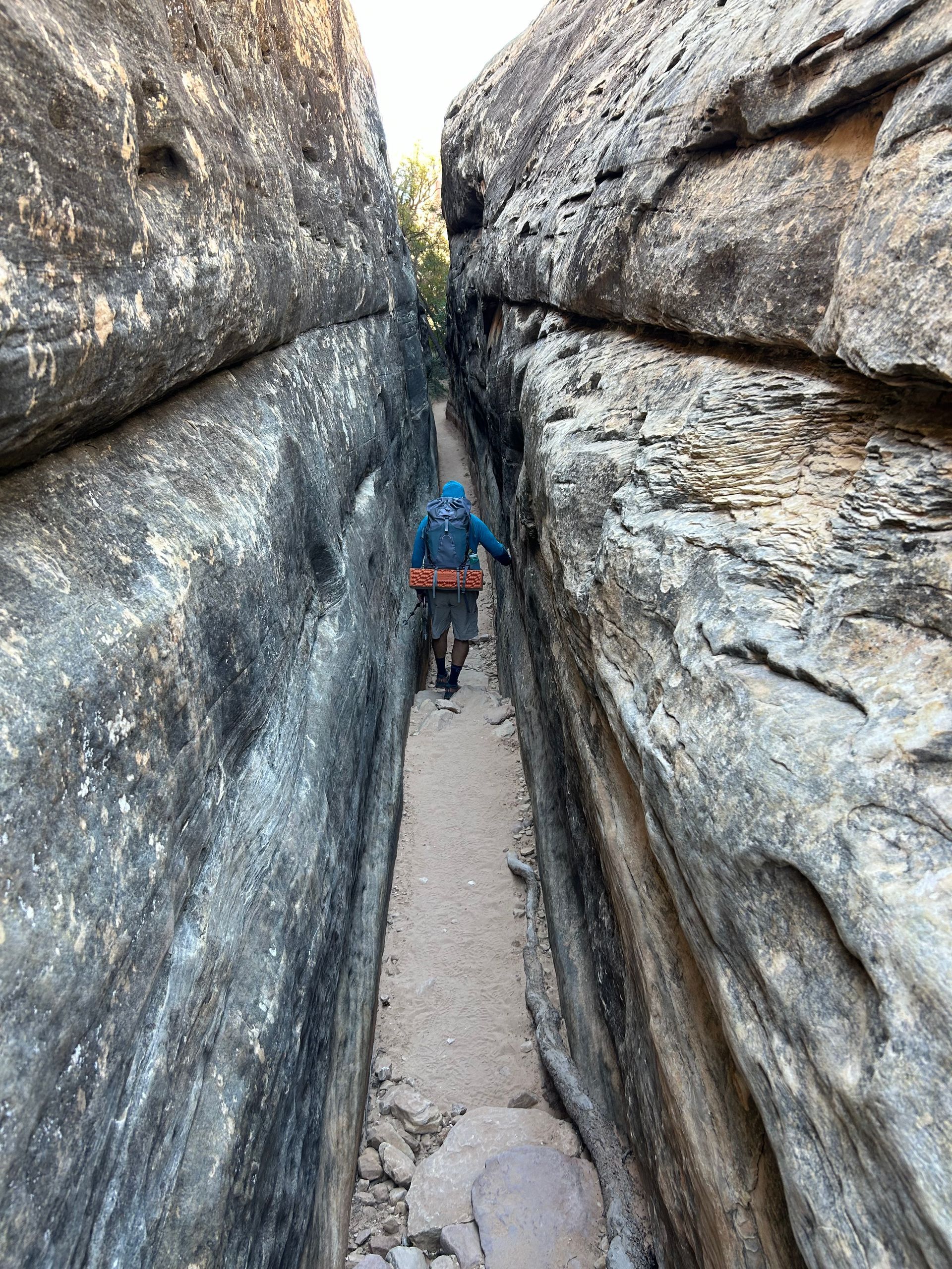 A person is walking through a narrow canyon between two rocks.