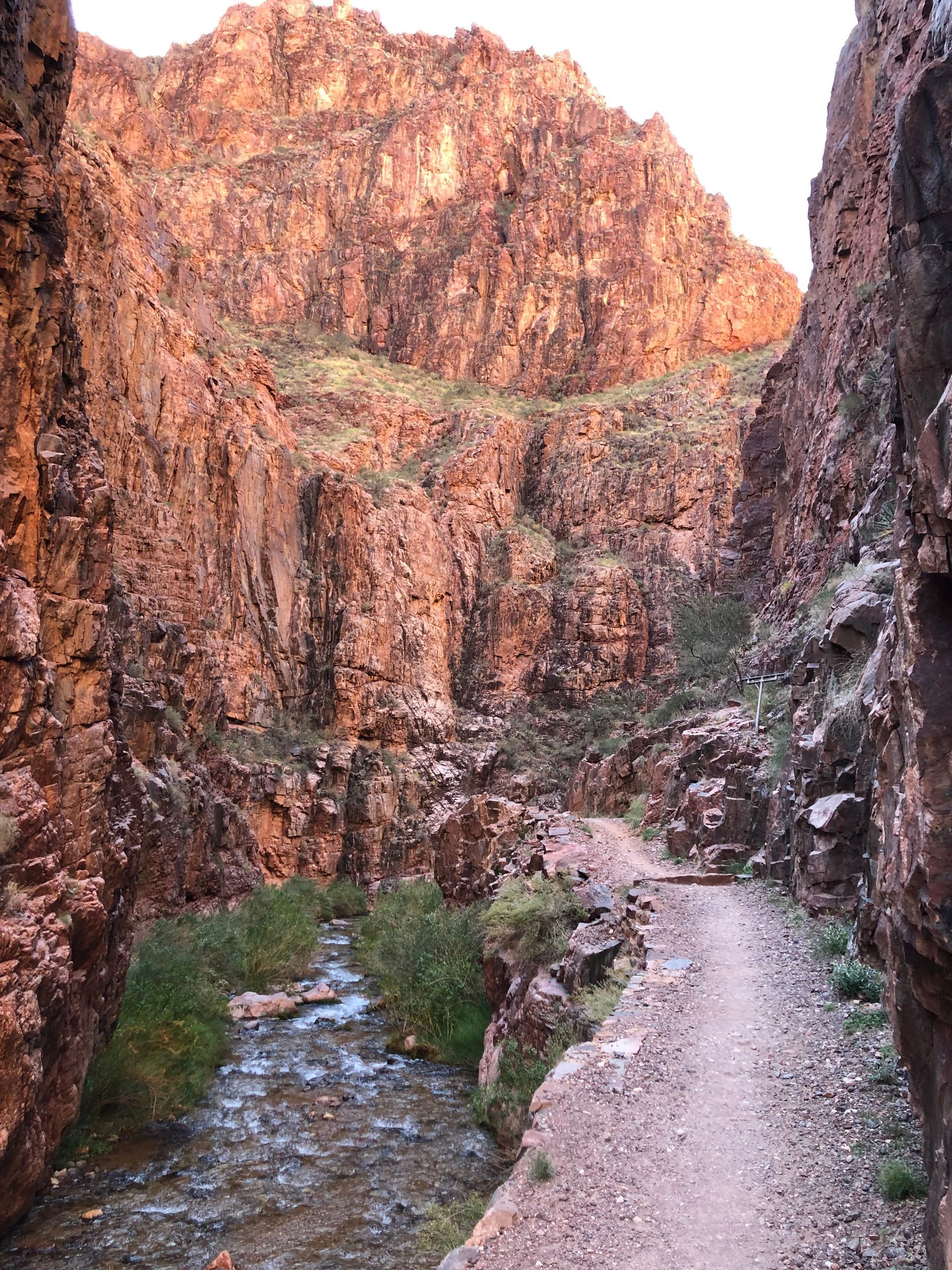 A dirt road going through a canyon with a river running through it.