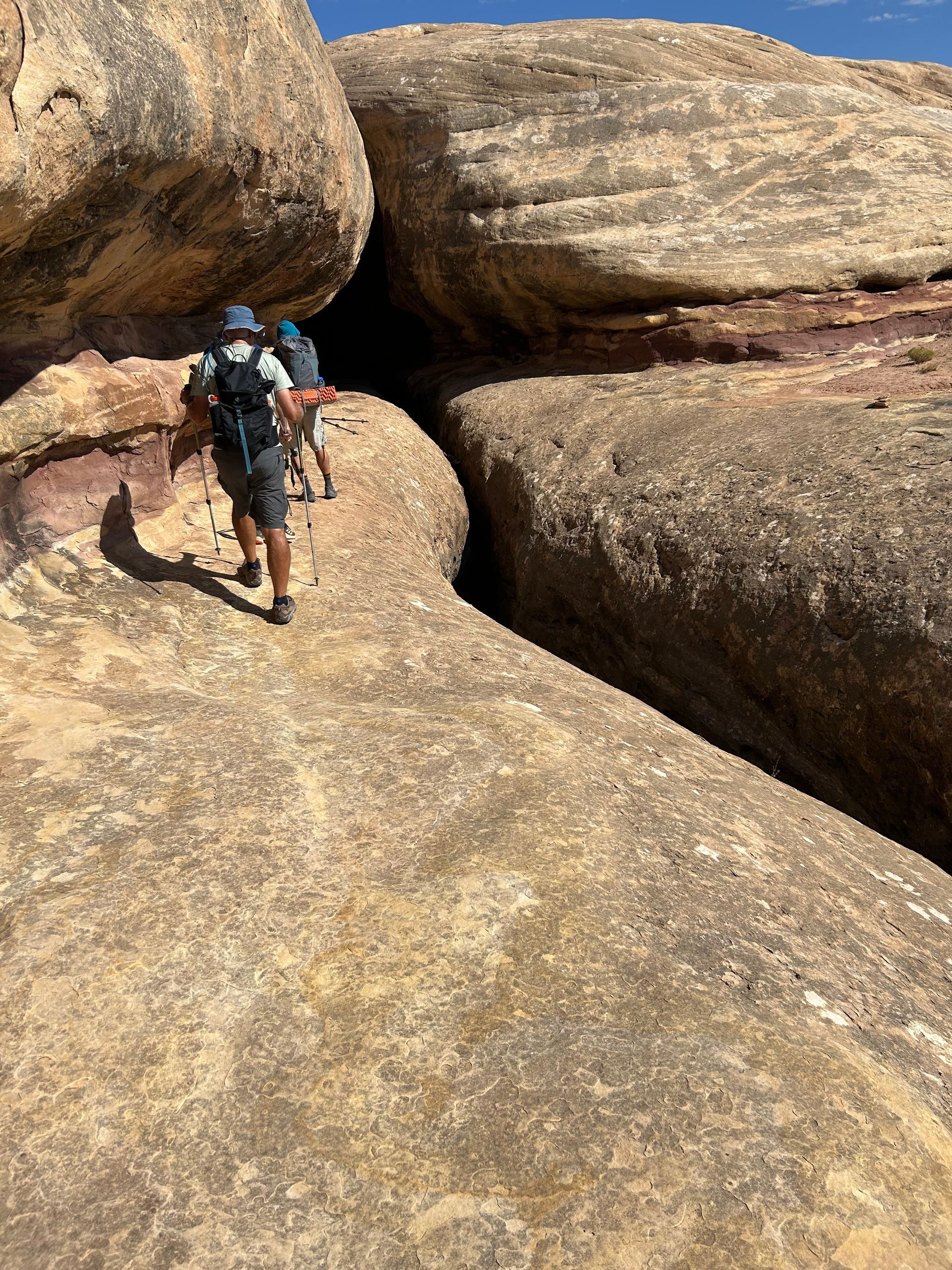 A man is walking through a cave between two large rocks.