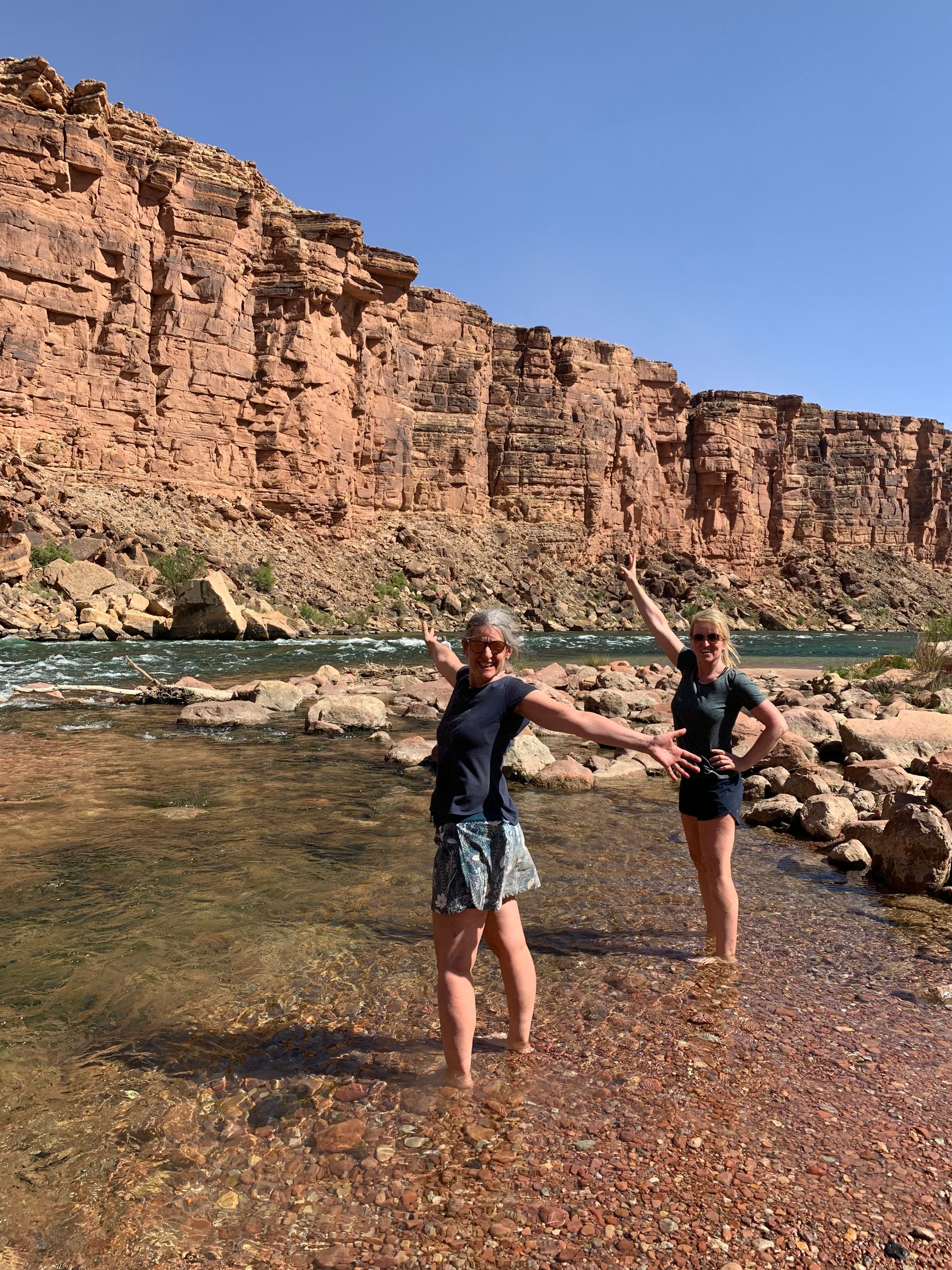 Two women are standing in a river with their arms outstretched.