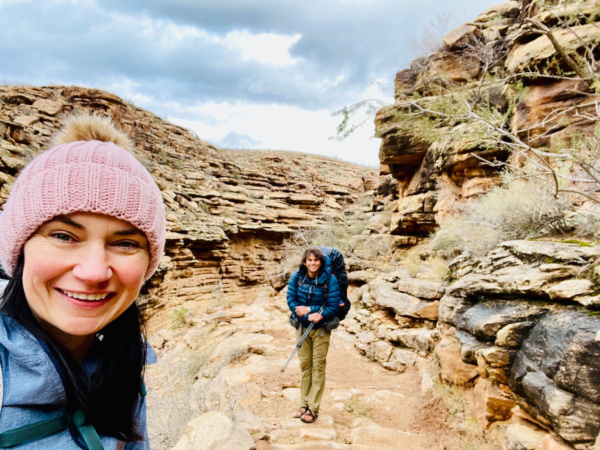 A woman in a pink hat is taking a selfie with another woman on a trail.