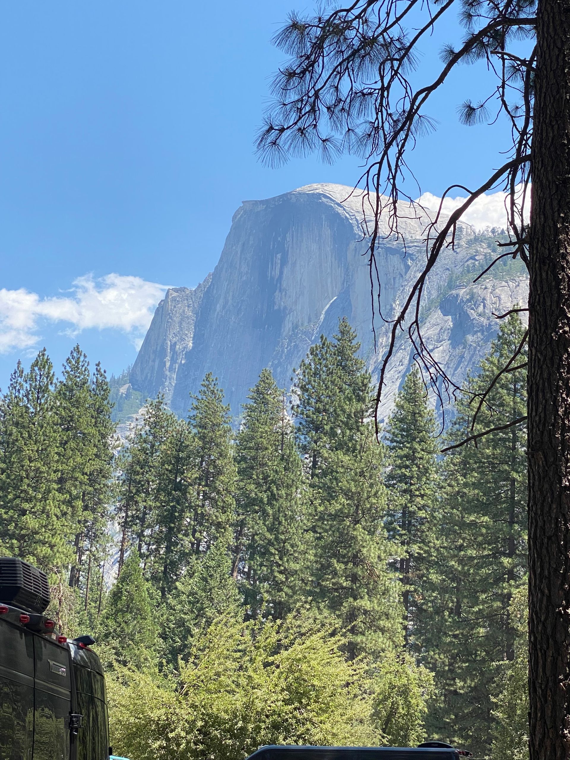 A car is parked in front of a mountain surrounded by trees.
