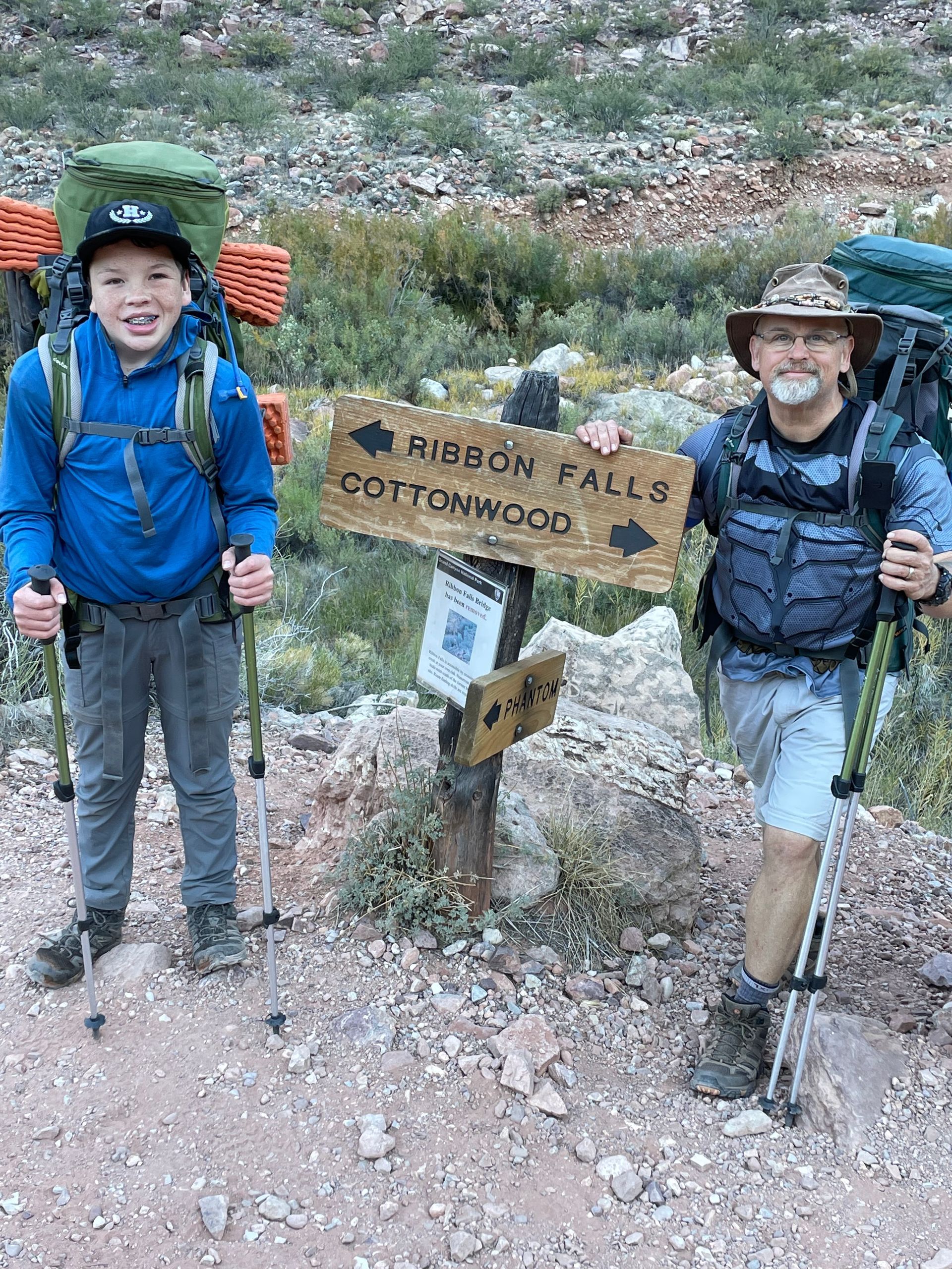 A man and a boy are standing next to a sign that says ribbon falls cottonwood.
