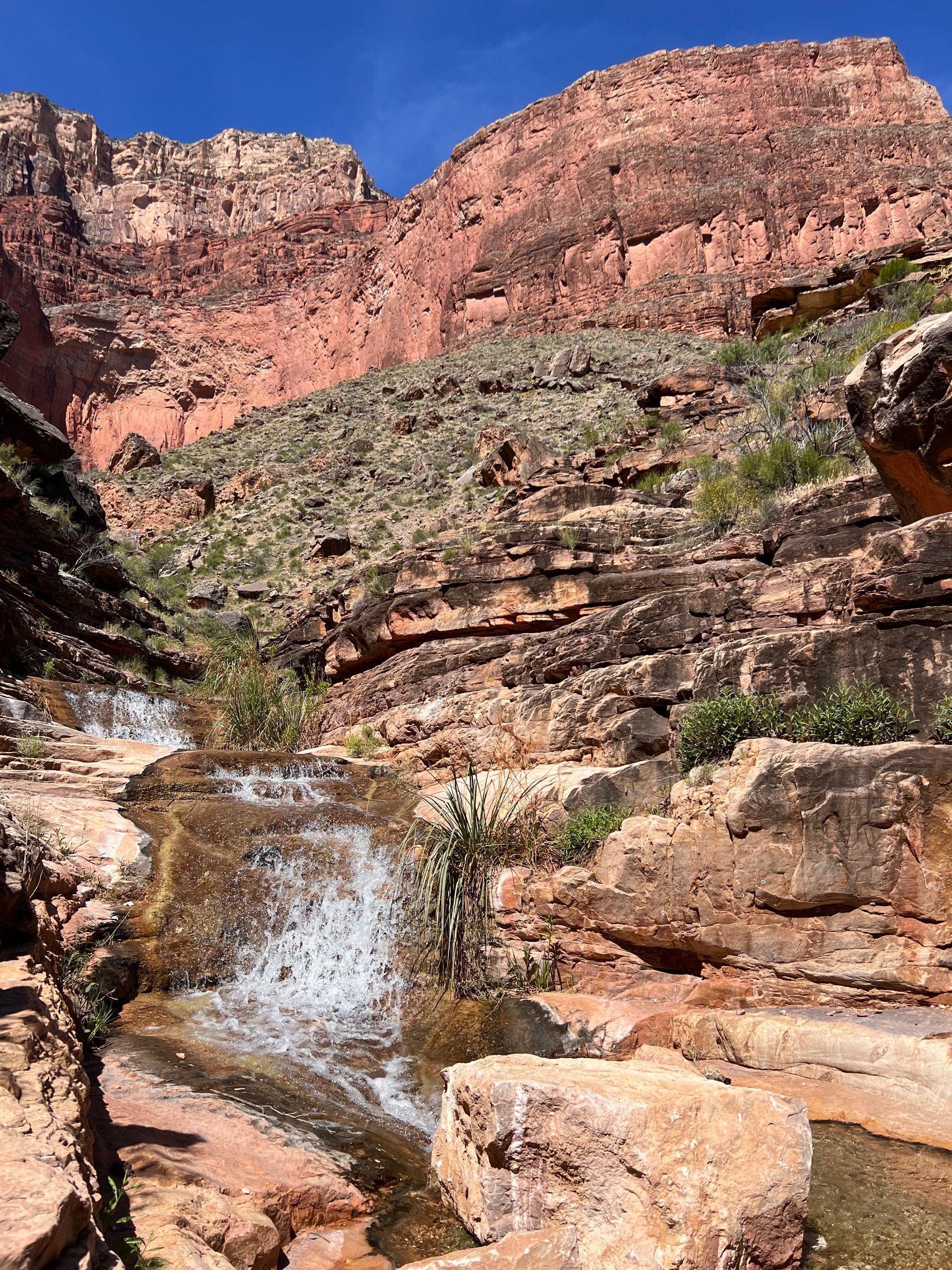 A small waterfall in the middle of a canyon with mountains in the background.