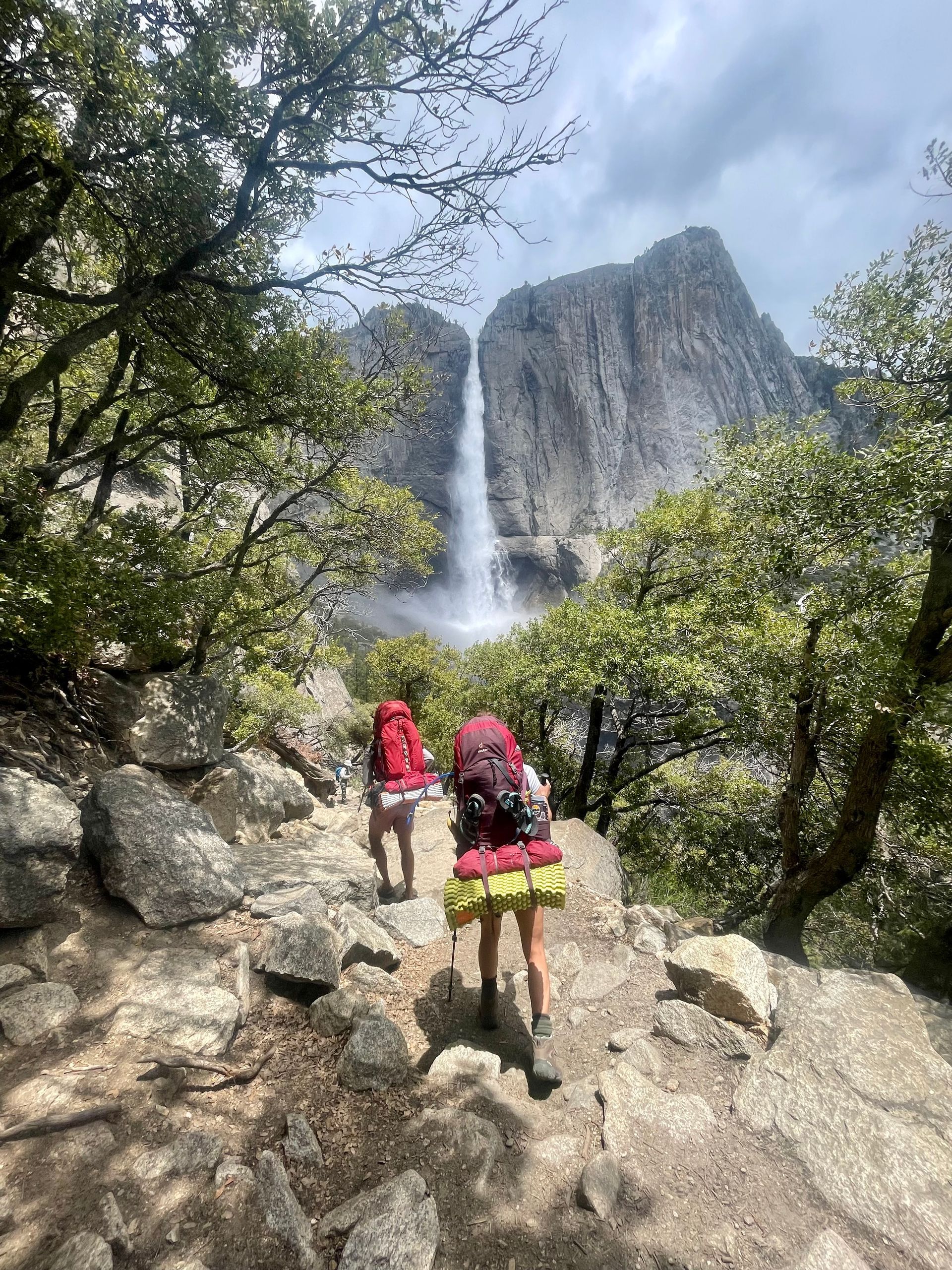 A couple of people are hiking up a mountain with a waterfall in the background.