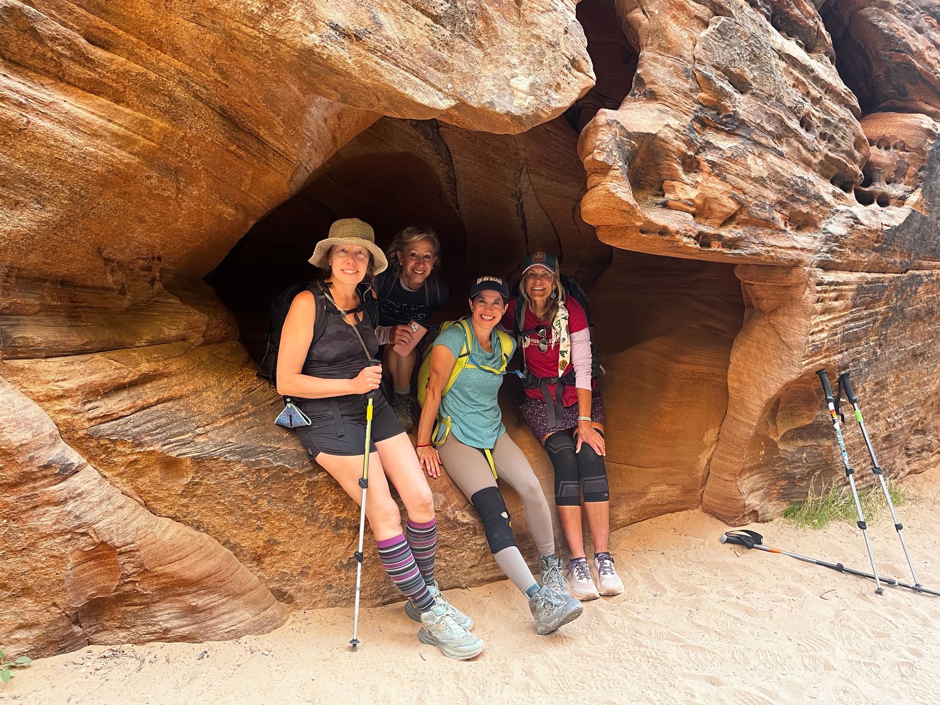 Group of hikers resting in a sandstone cave; various colors of clothing; sunny day.