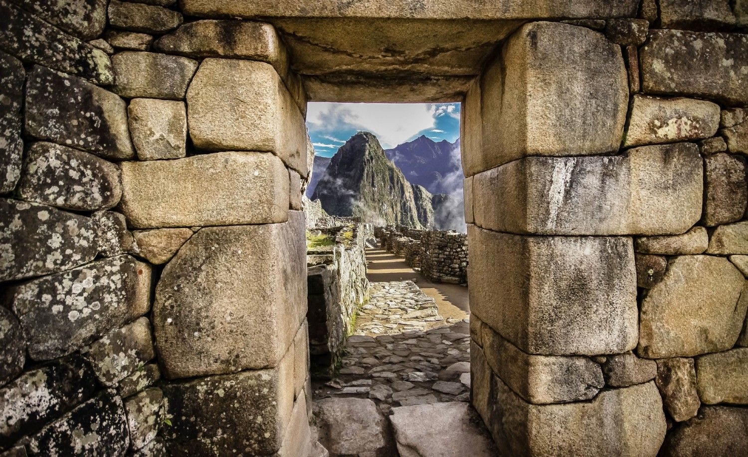 Stone doorway framing a view of Machu Picchu's mountain peaks, featuring stonework and blue sky.