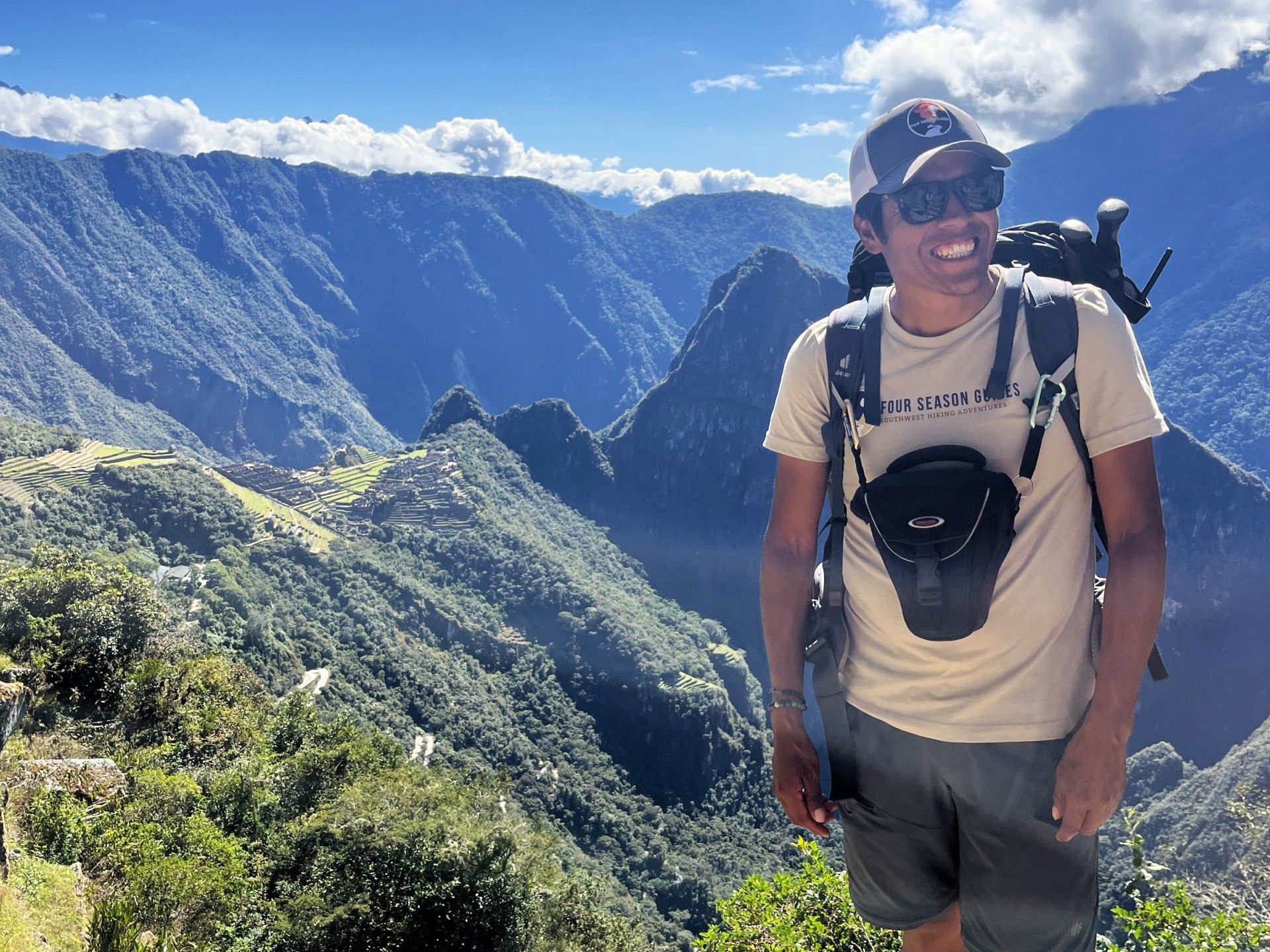 Hiker standing on a mountain overlook with a backpack, blue sky, and deep green valleys below