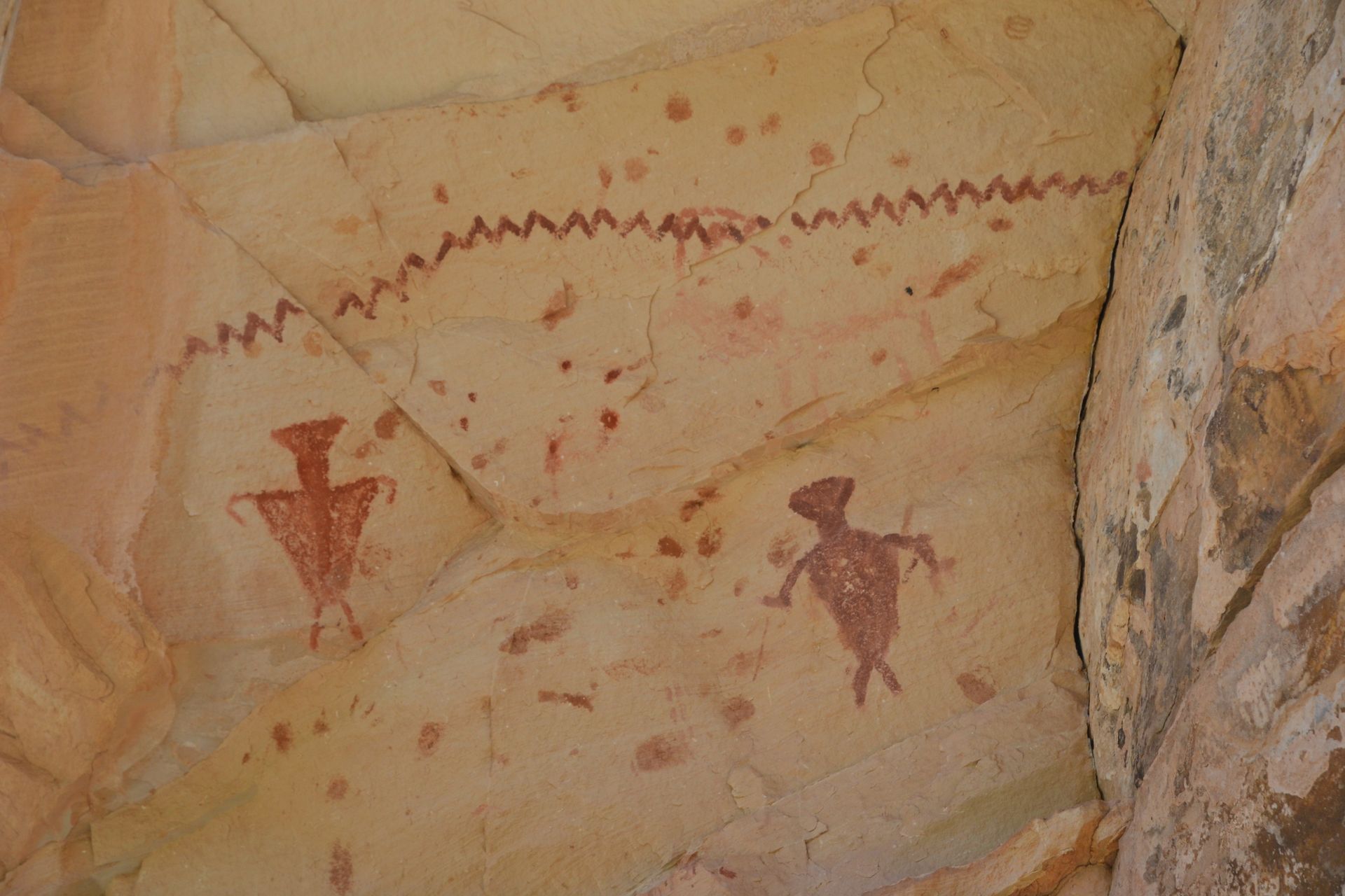 Cave painting with two red figures and a wavy line.