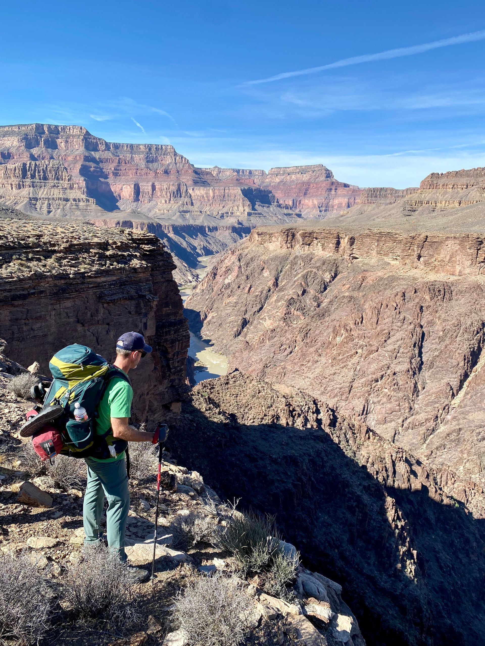A man with a backpack is standing on a cliff overlooking a canyon.
