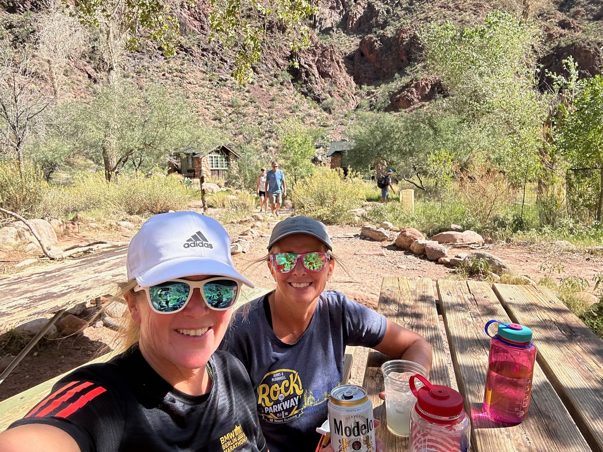 Two women are sitting at a picnic table with drinks.