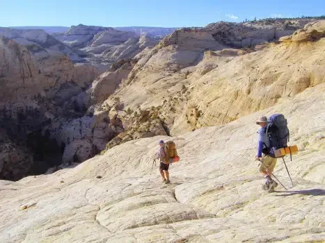 Two people with backpacks are hiking up a mountain.