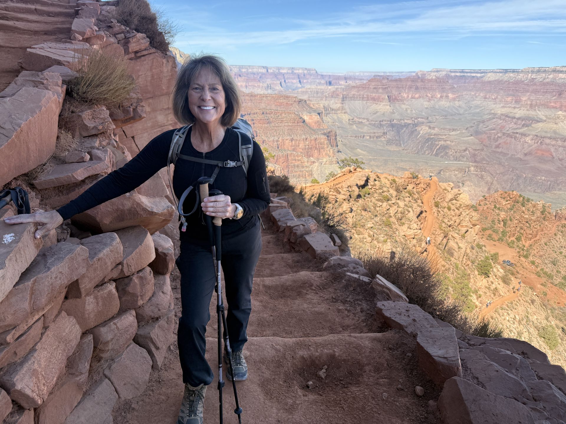 Woman hikes down steep stone steps on a canyon trail, holding hiking poles.