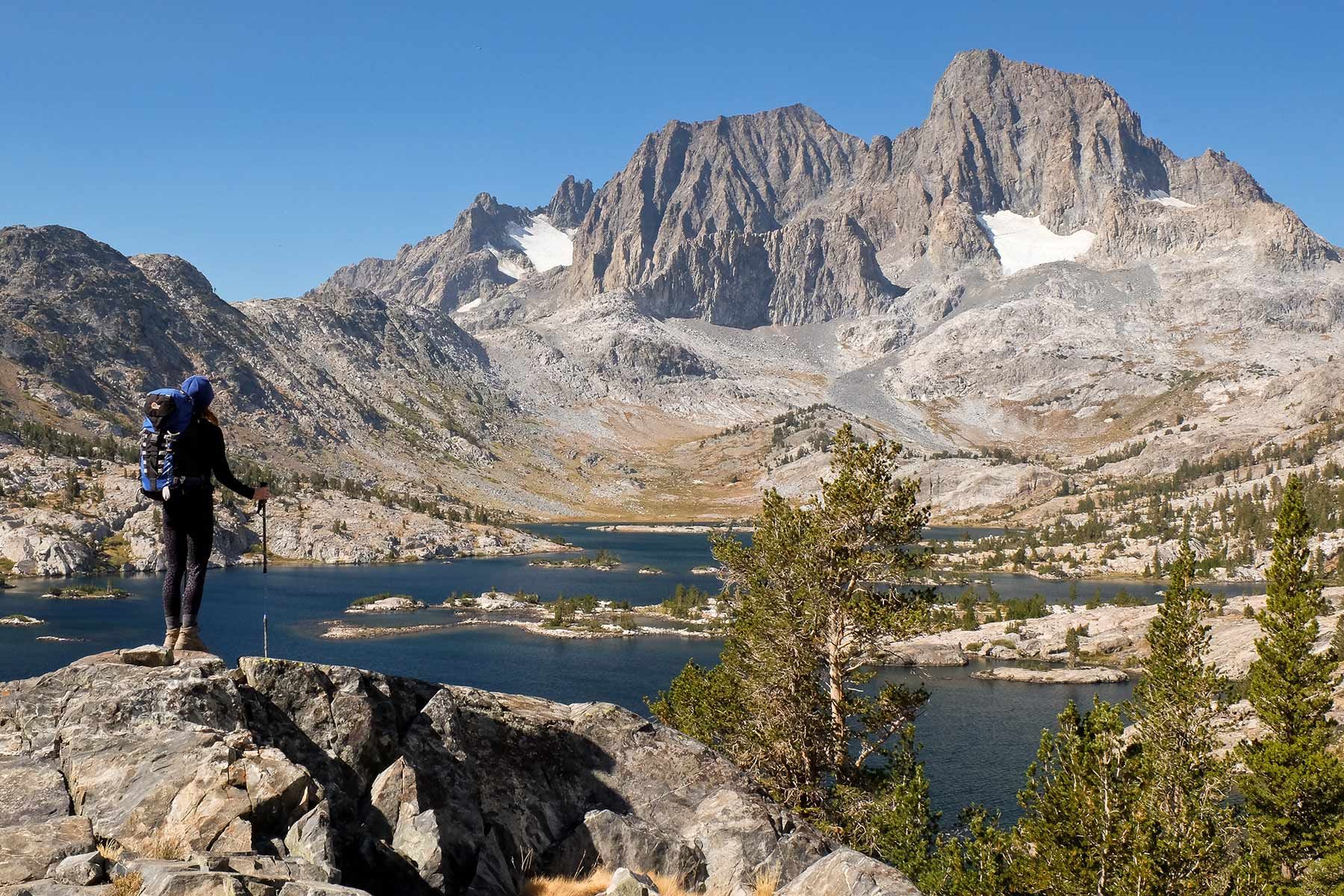 Hiker overlooking a blue alpine lake and rugged mountain peaks under a clear sky