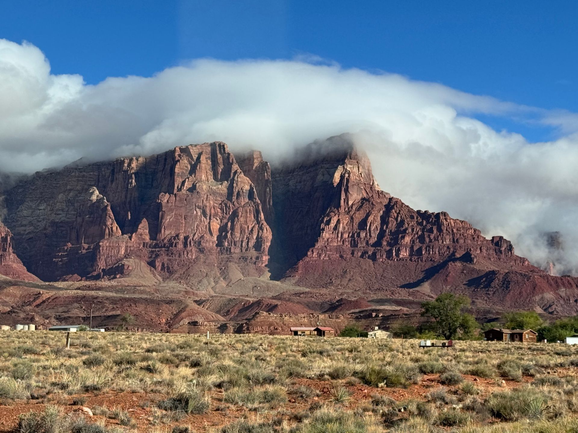 Red mountain peaks partially obscured by white clouds over a field with low vegetation.