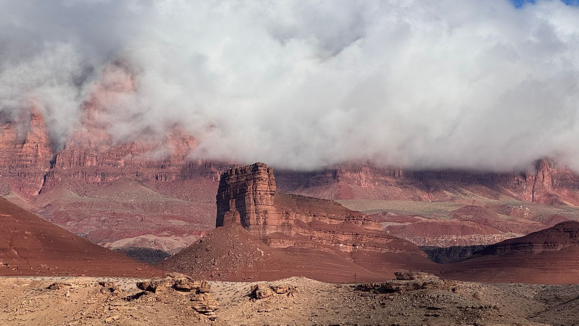 Red rock formations under cloudy sky. Desert landscape with butte in the center.