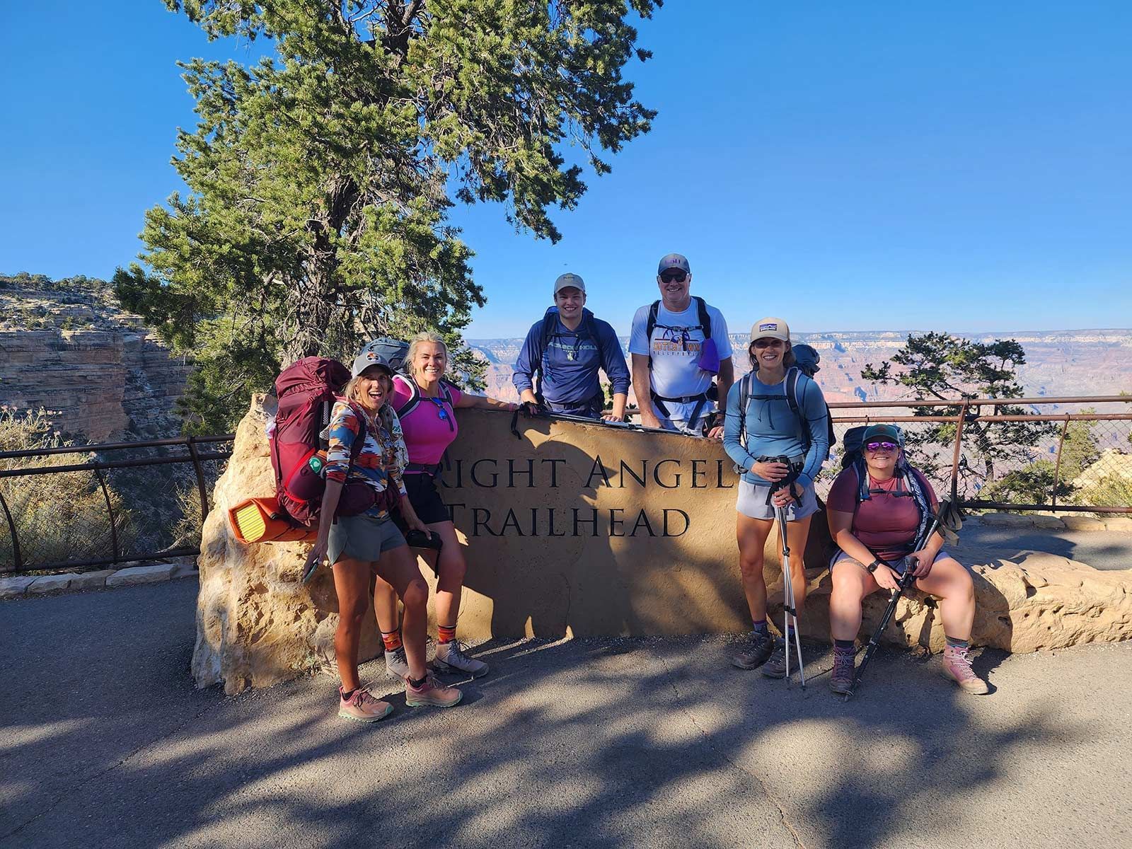 Hikers posing on a rock wall at the Bright Angel Trailhead on a sunny day.