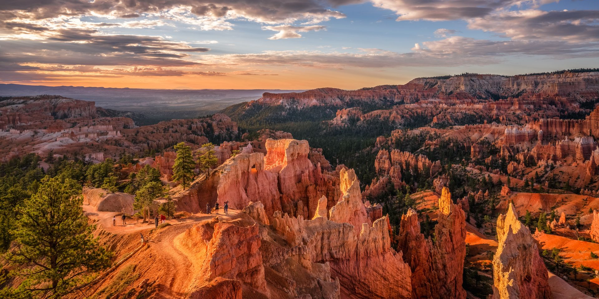 Sunlit orange hoodoos and canyon cliffs at sunset under a colorful sky