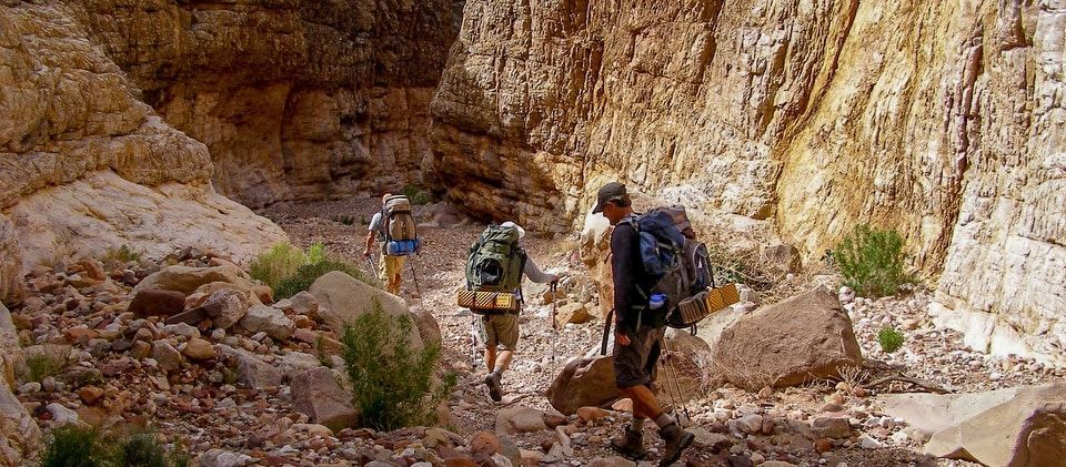 A group of people with backpacks are walking through a rocky area.