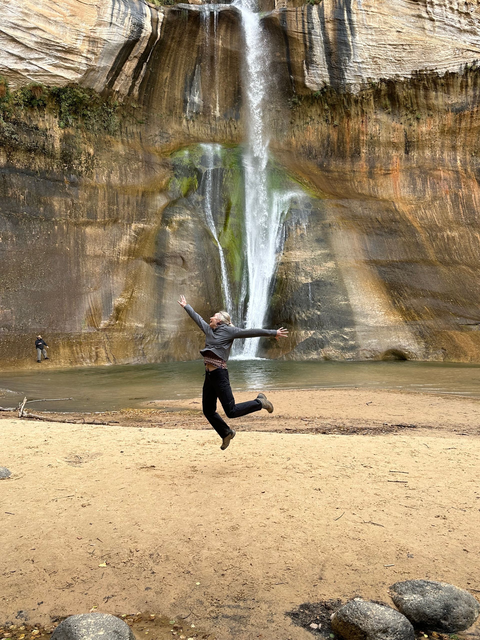A woman is jumping in the air in front of a waterfall.