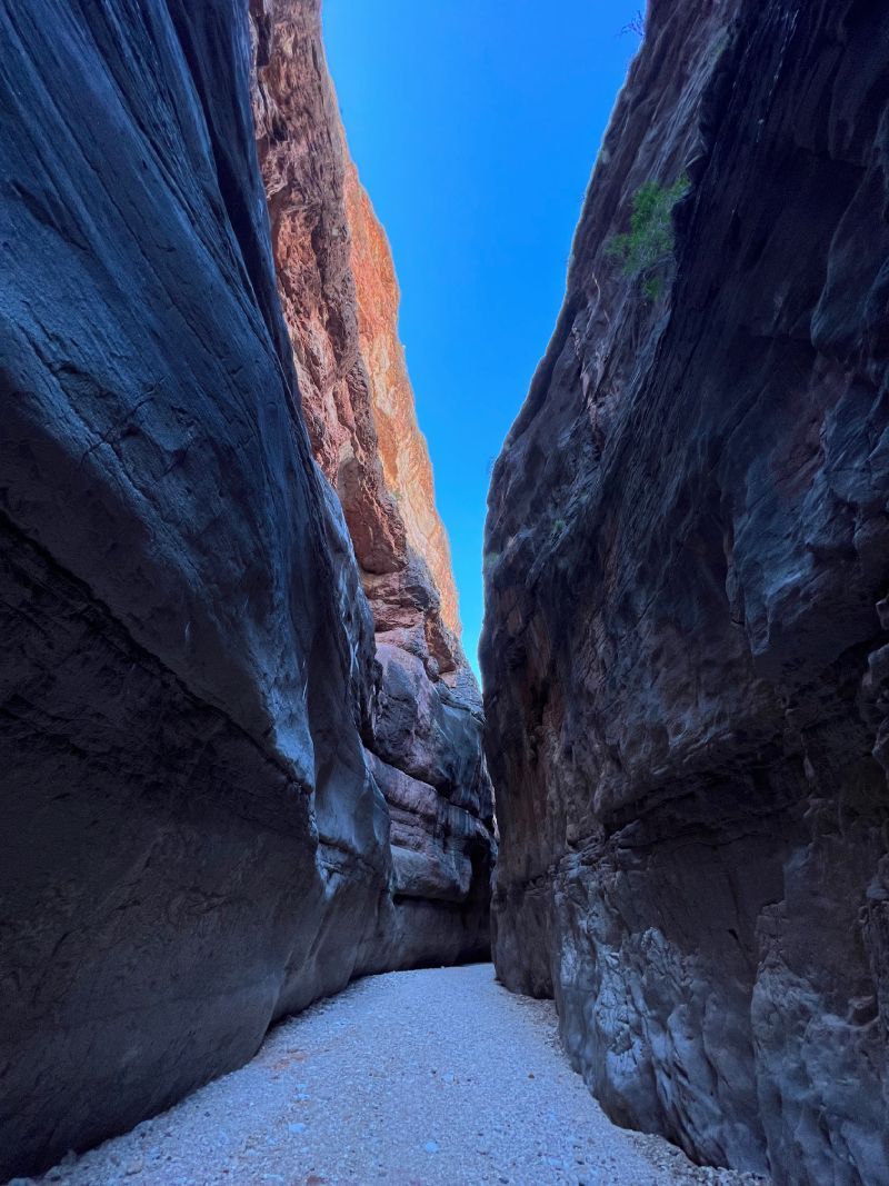 Narrow canyon with towering dark rock walls and a snowy path leading into the distance