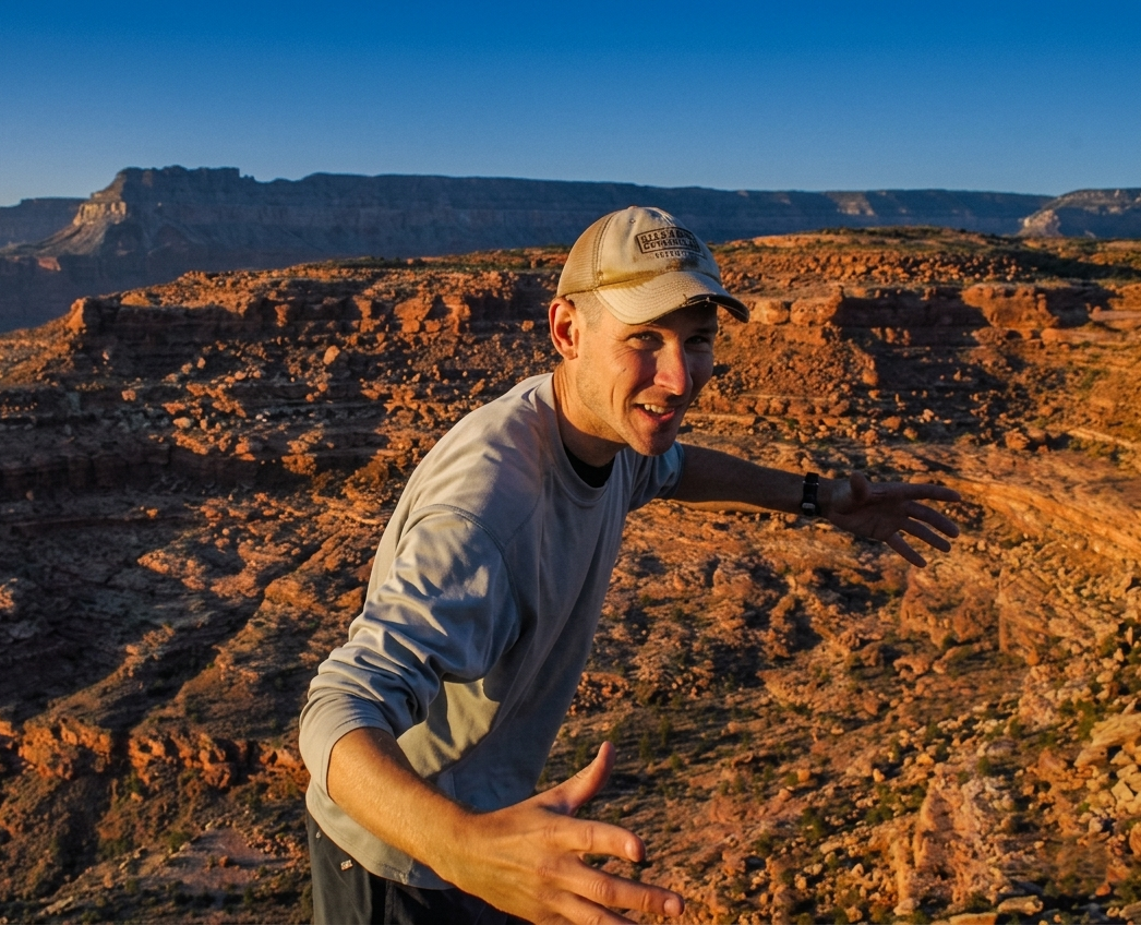 A man in a ball cap is standing in grand canyon near sunset
