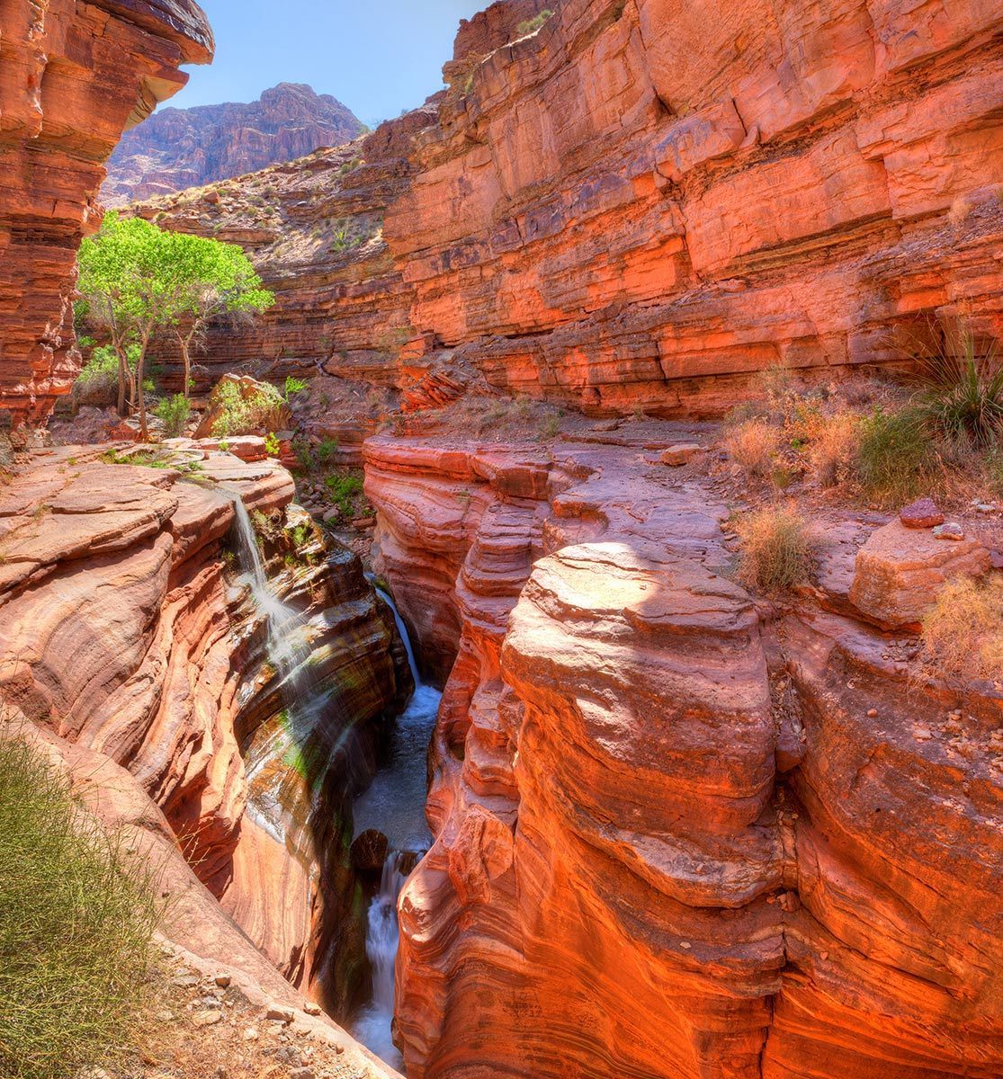 Narrow canyon with red rock walls and a small waterfall flowing through a rocky gorge