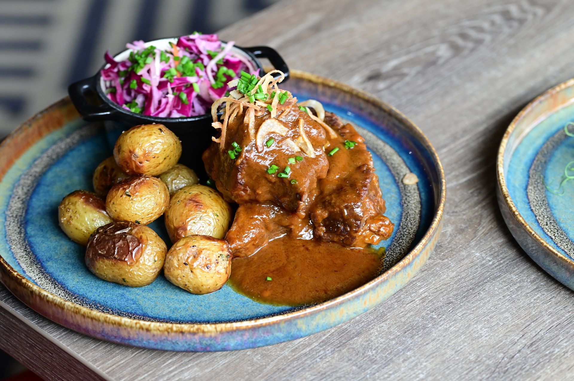 Braised meat with roasted potatoes and purple slaw on a blue plate on a wooden table