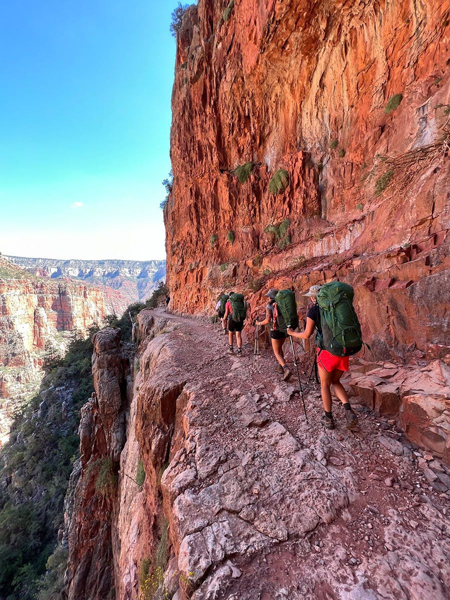 People hike along a narrow path along a canyon wall