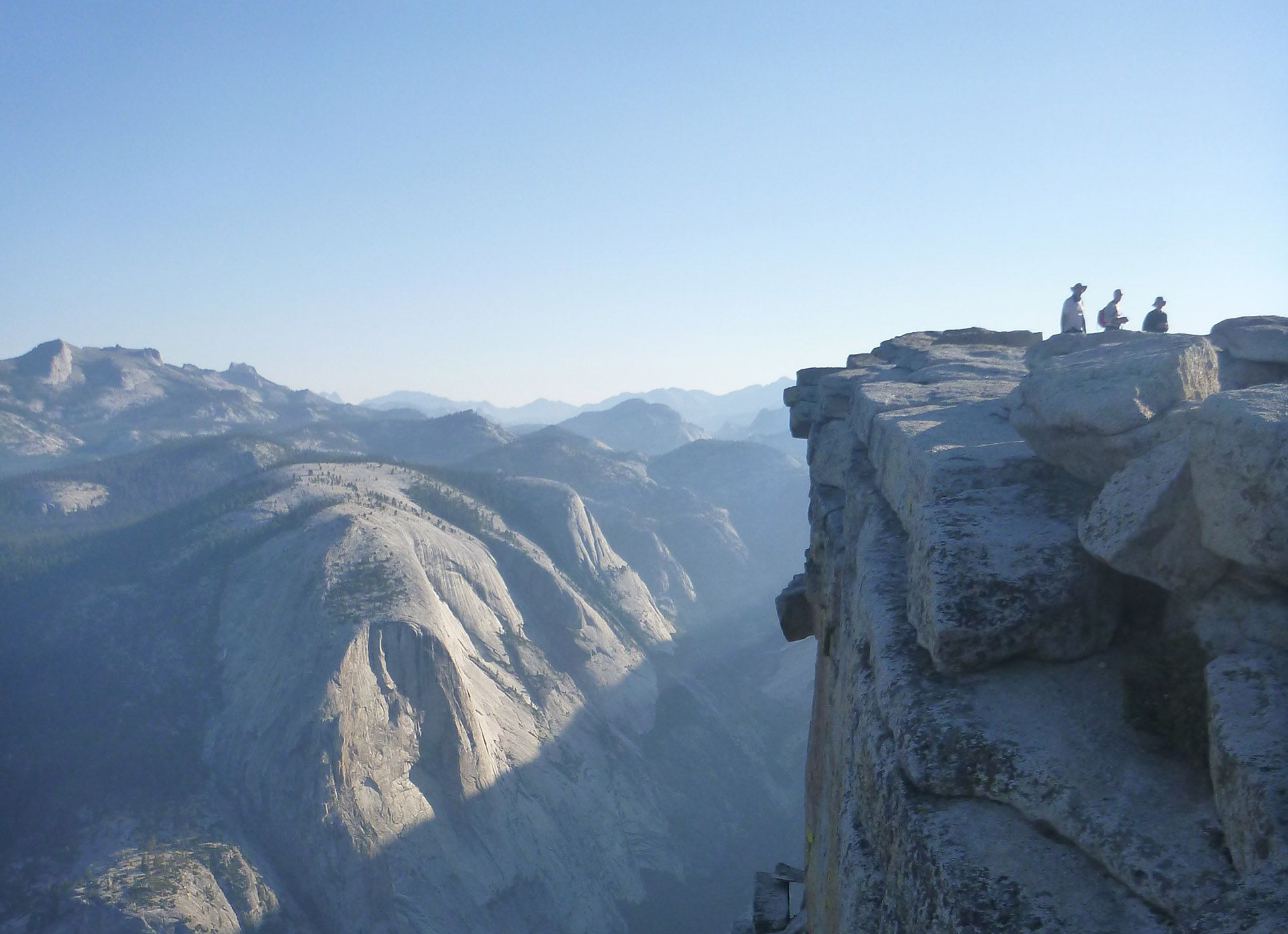 Snowy mountain ridge with a cliff overlook and hikers silhouetted against a hazy blue valley