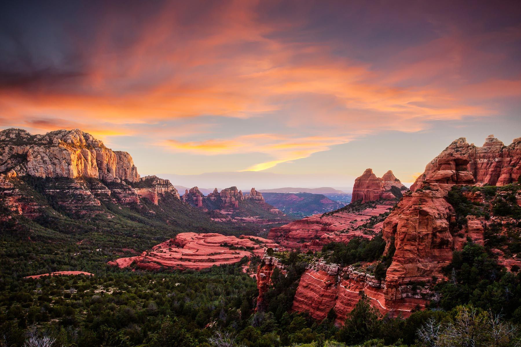 Sunset over red sandstone cliffs and a green valley beneath a colorful pink-orange sky