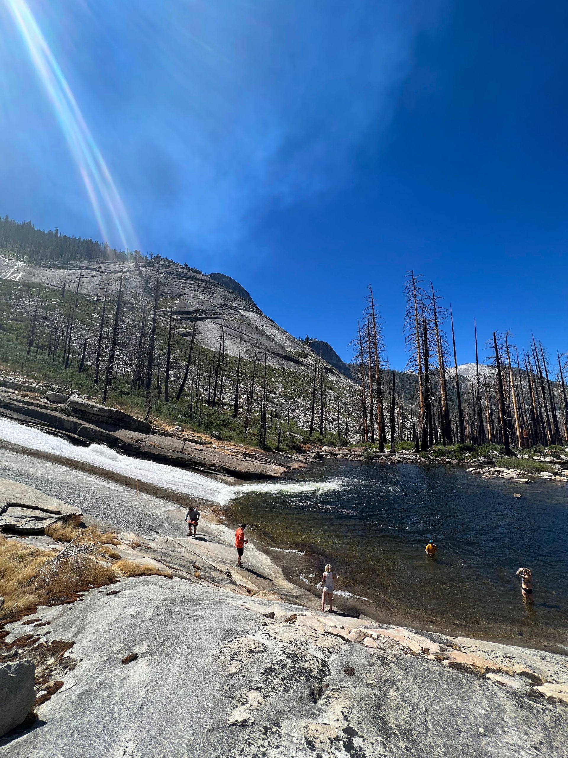 A group of people are standing on the shore of a lake in the mountains.
