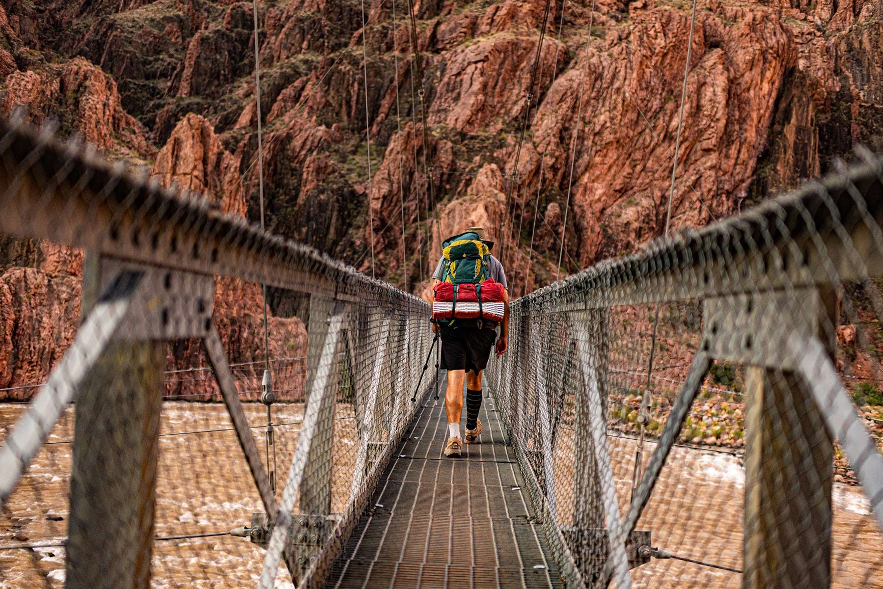A person wearing a backpack crosses a narrow bridge