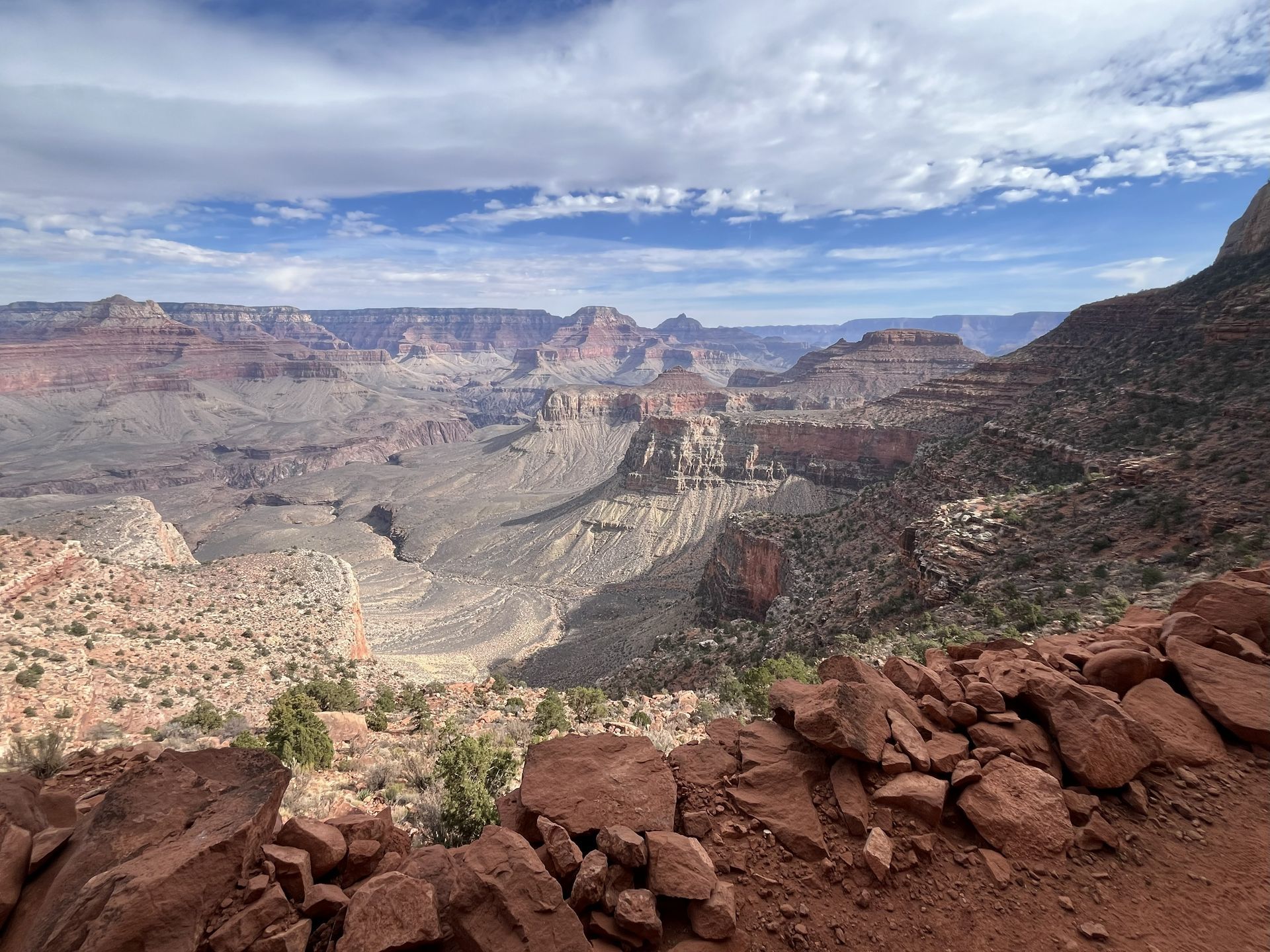Grand Canyon vista under a partly cloudy sky. Rugged red rock formations and canyons dominate the landscape.