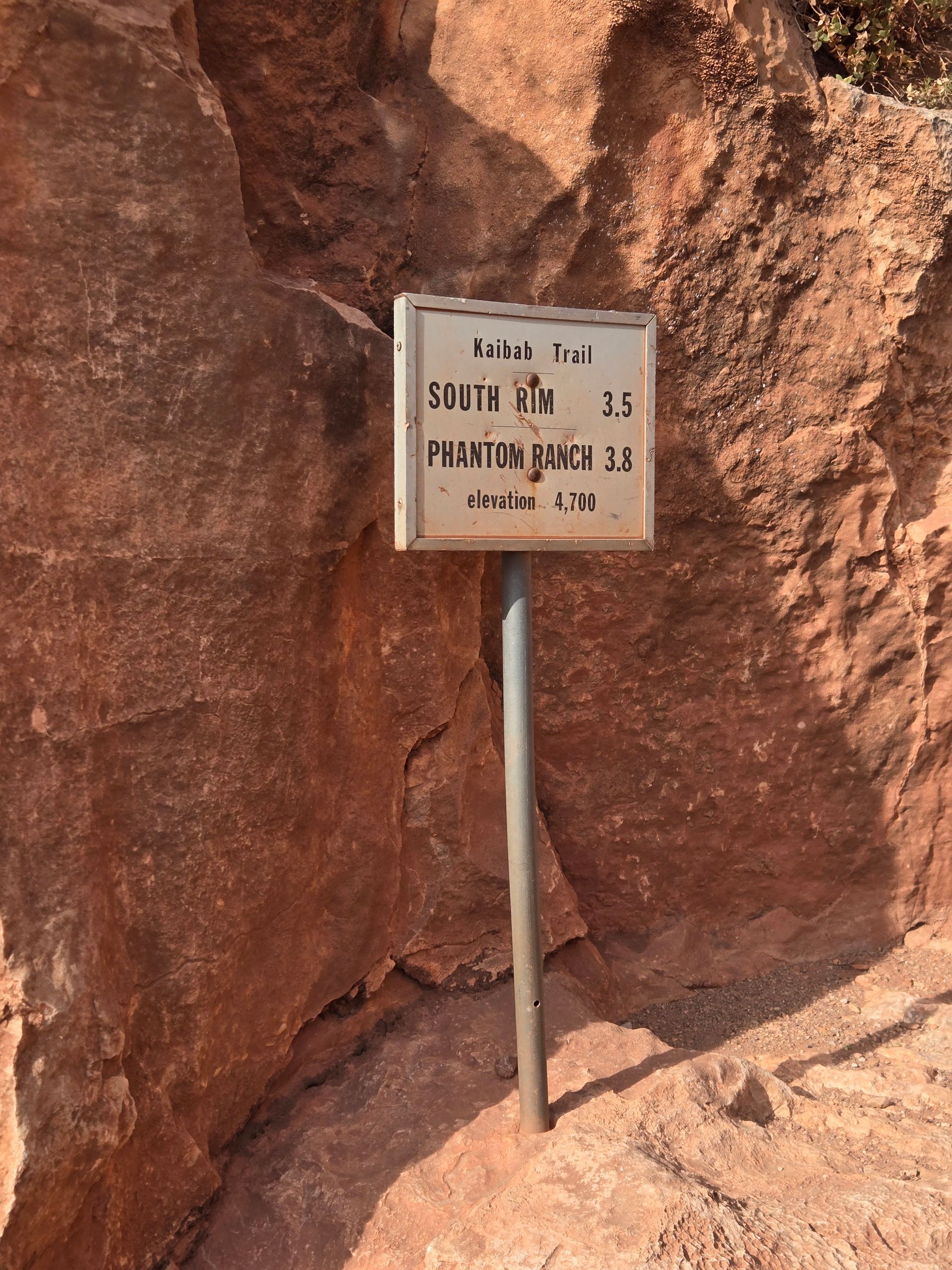 Signpost on red rock reads: Camp Out, South Rim 2.5, Phantom Ranch 3.8 miles.