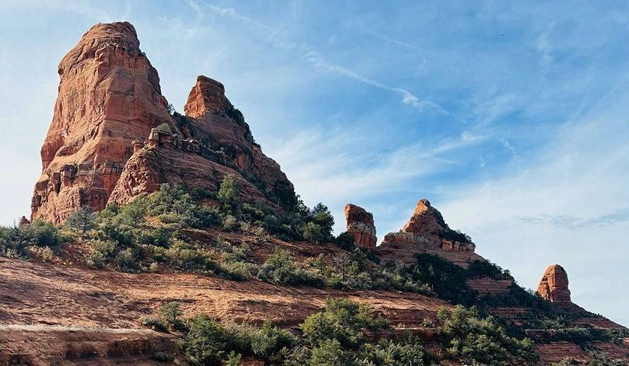 Red sandstone rock formations rising above scrubby desert terrain under a blue sky.