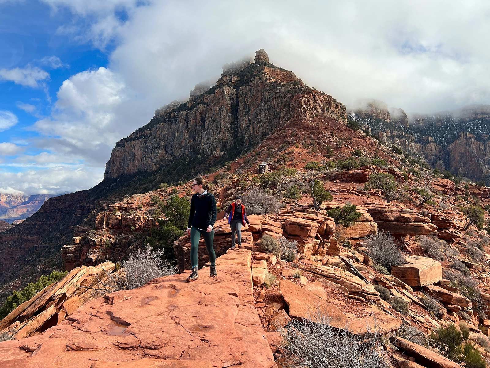 Hiker on rocky mountain trail with dramatic cliffs and cloudy sky in the background